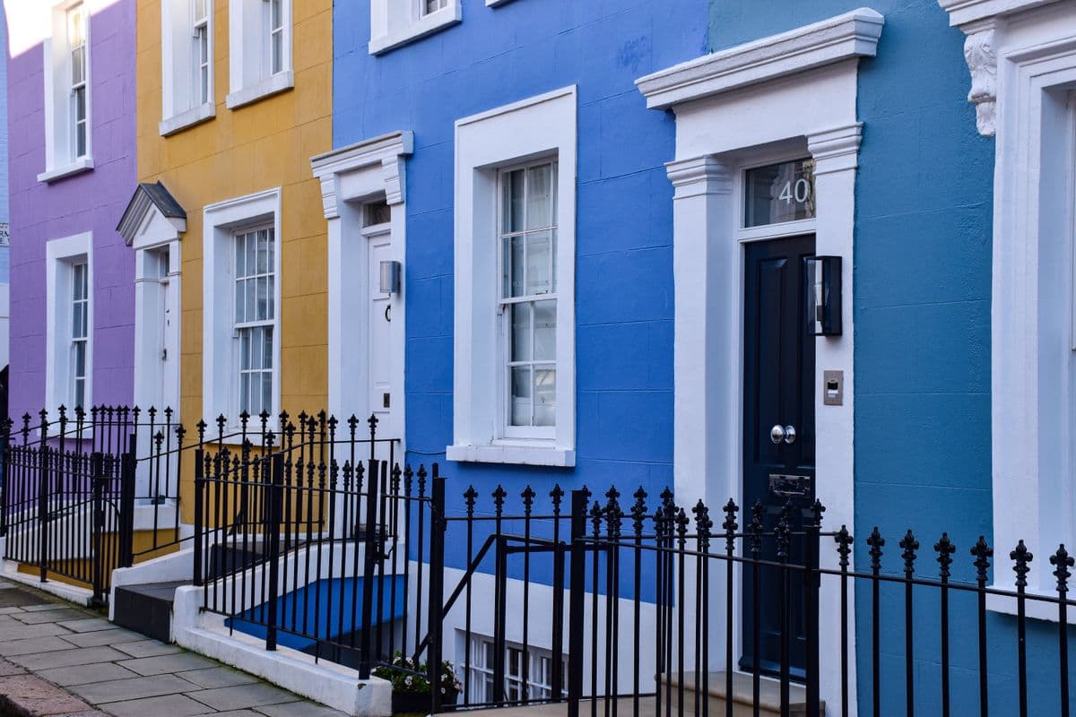 Row of brightly painted London terraced houses with black iron railings and a navy front door